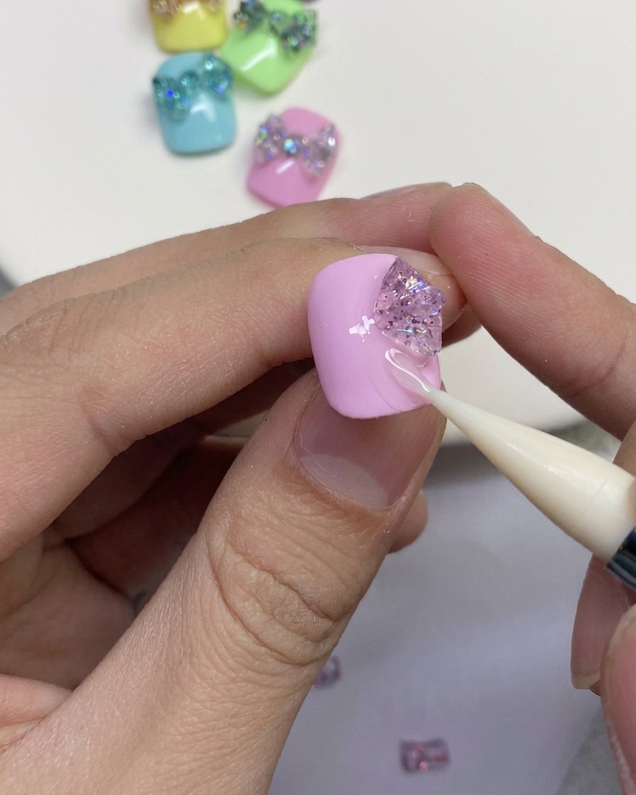Gros plan montrant un outil en silicone façonnant des morceaux de gel pailleté pour former les boucles extérieures dun nœud papillon sur un ongle rose.