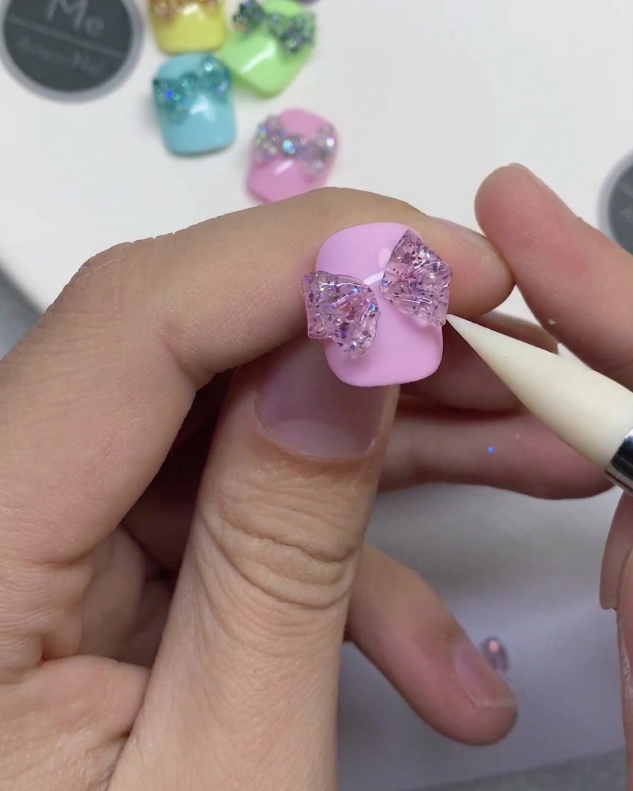 Gros plan dun outil en silicone blanc senfonçant dans une bande centrale de gel pailleté pour relier deux boucles de nœud sur un ongle rose.