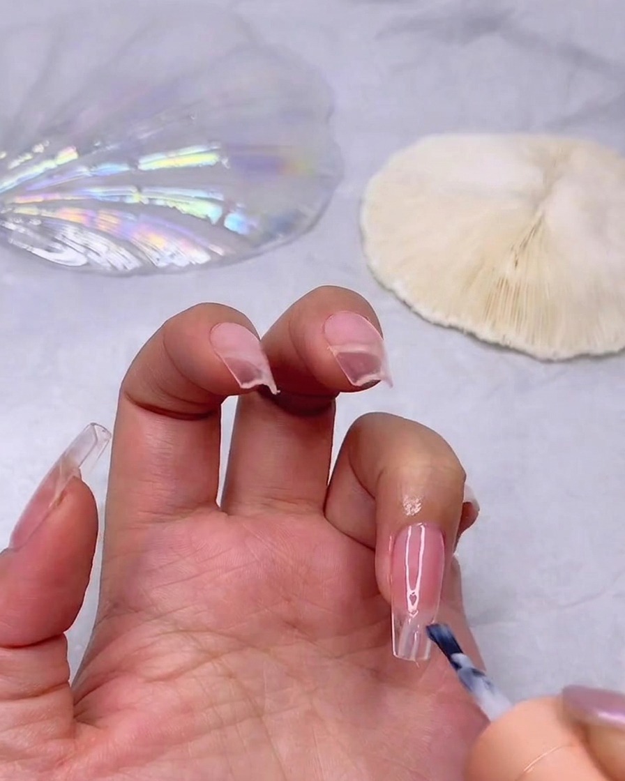 Un pinceau appliquant une couche de vernis gel blanc laiteux sur la pointe dun ongle rosé pour débuter leffet ombré.