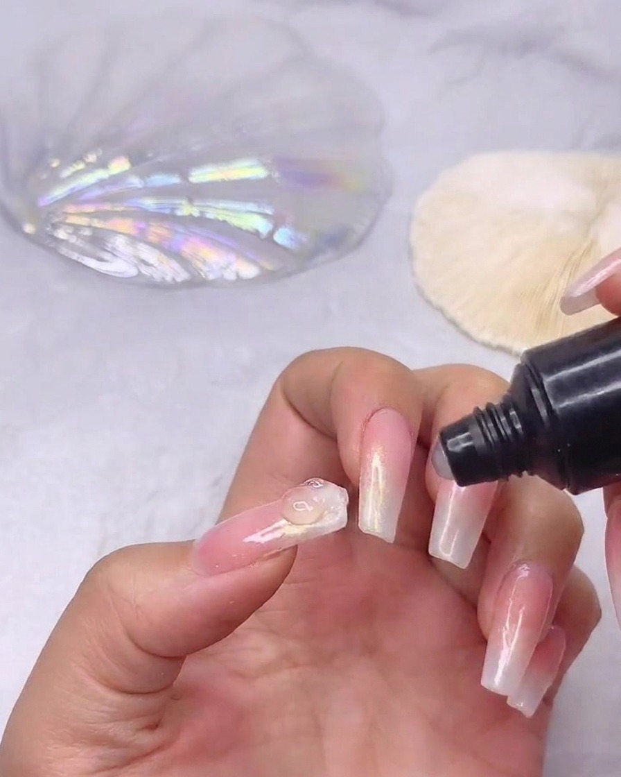 Un tube de gel adhésif pour strass déposant une petite goutte de colle transparente au centre dun ongle dégradé préparé.