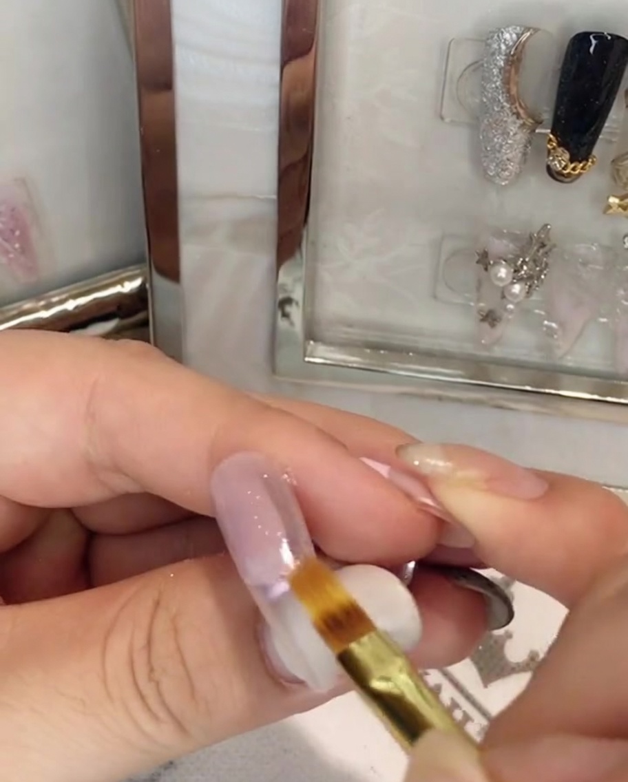 Un pinceau plat pour ongles estompant le gel rose vers le bas au centre de la plaque de longle.
