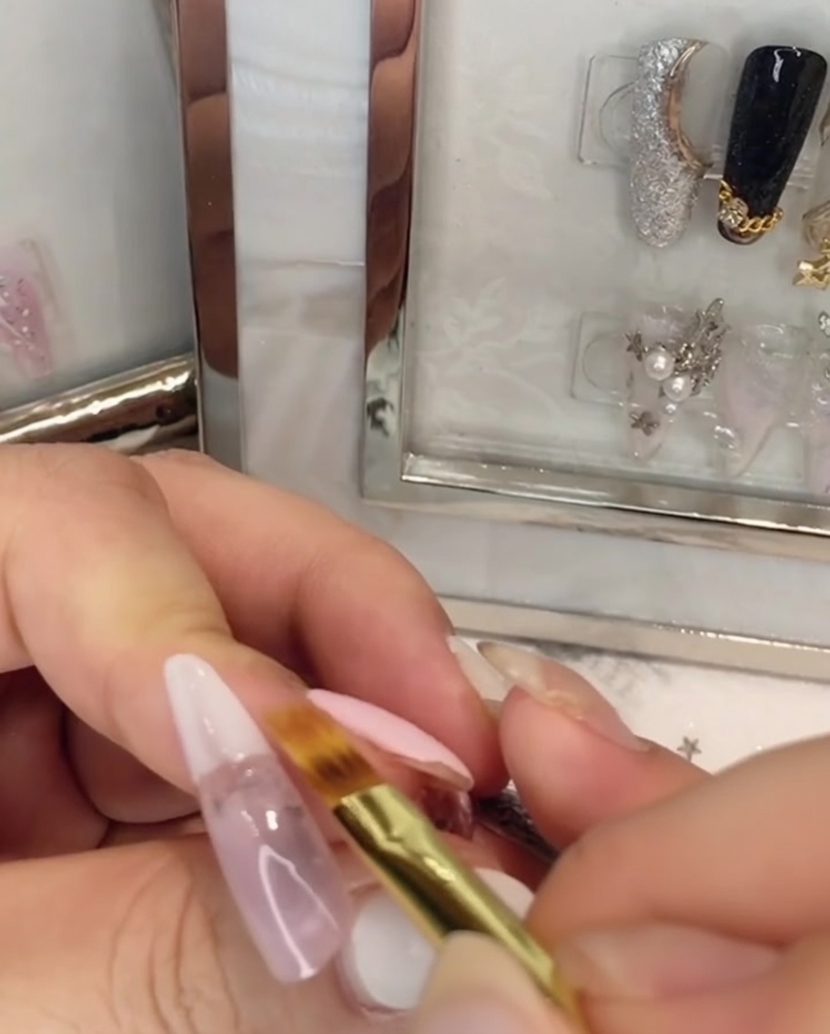 Un pinceau plat estompant le vernis gel blanc vers le haut dans le gel rose sur longle.