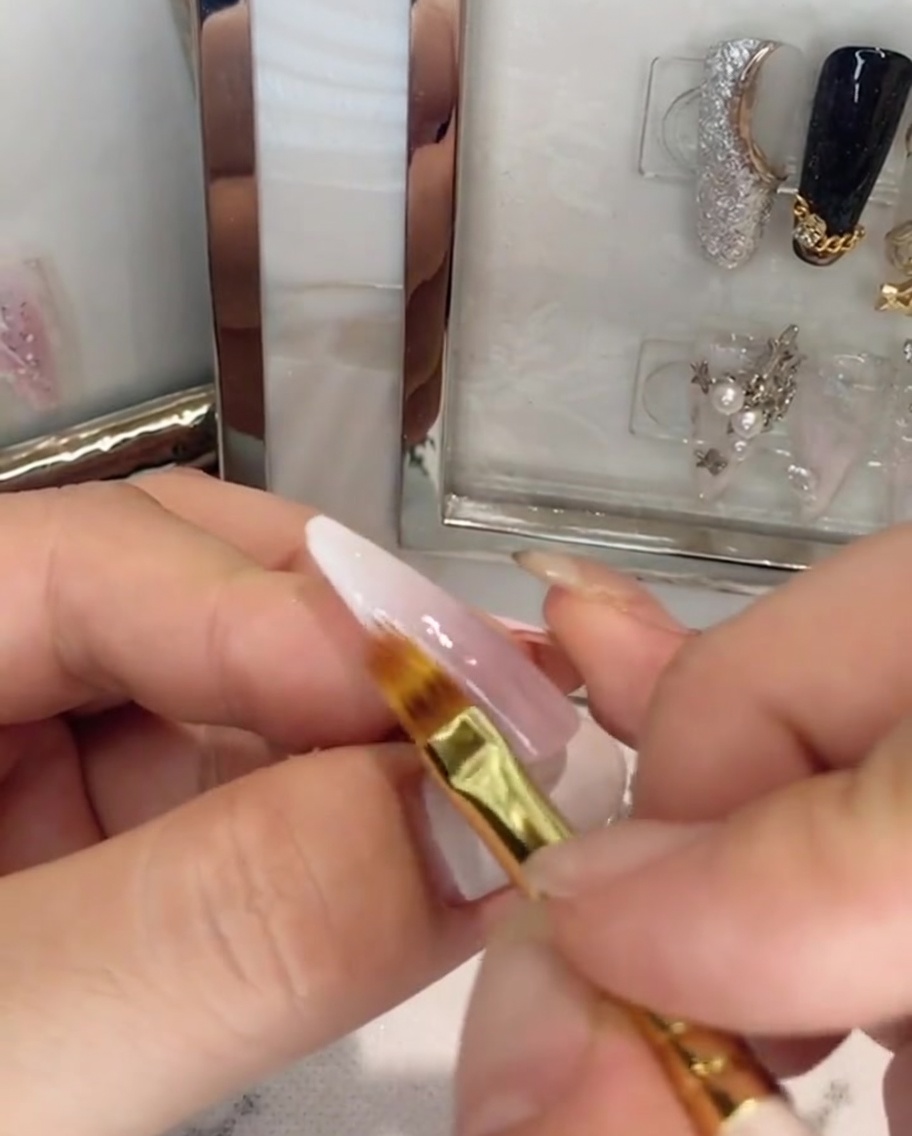 Un pinceau appliquant un top coat transparent sur un ongle ombré rose et blanc.