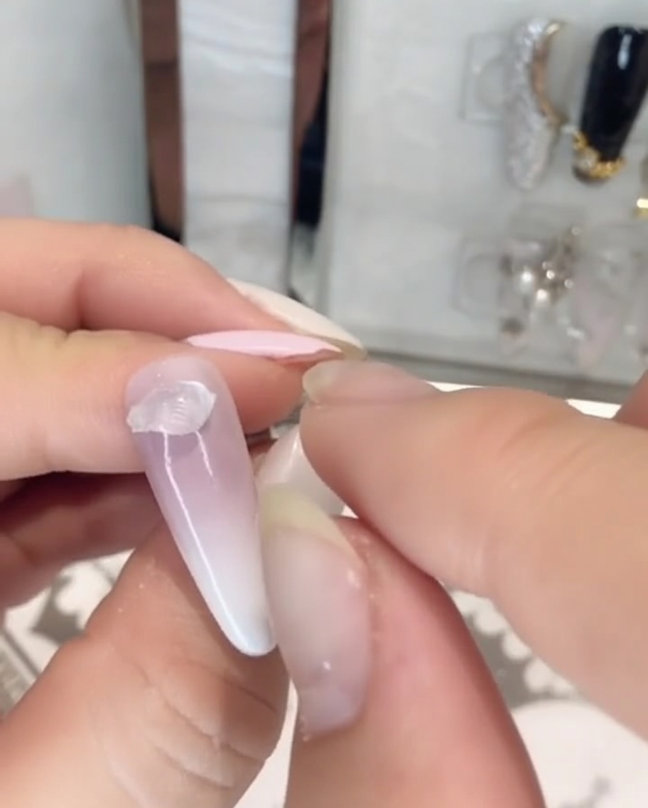 Des doigts déposant une portion de colle à strass solide transparente et épaisse à la base dun ongle peint.