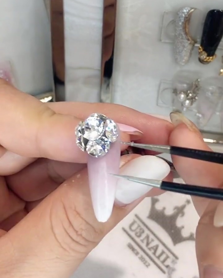 Une paire de pinces de précision ajustant des cristaux individuels dans une grande cascade de strass sur un ongle.