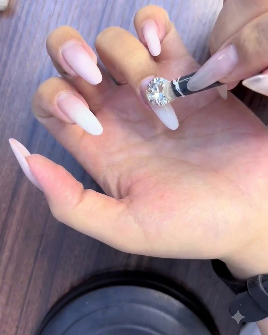 Un outil de préhension plaçant un grand strass diamant étincelant au centre dun ongle.