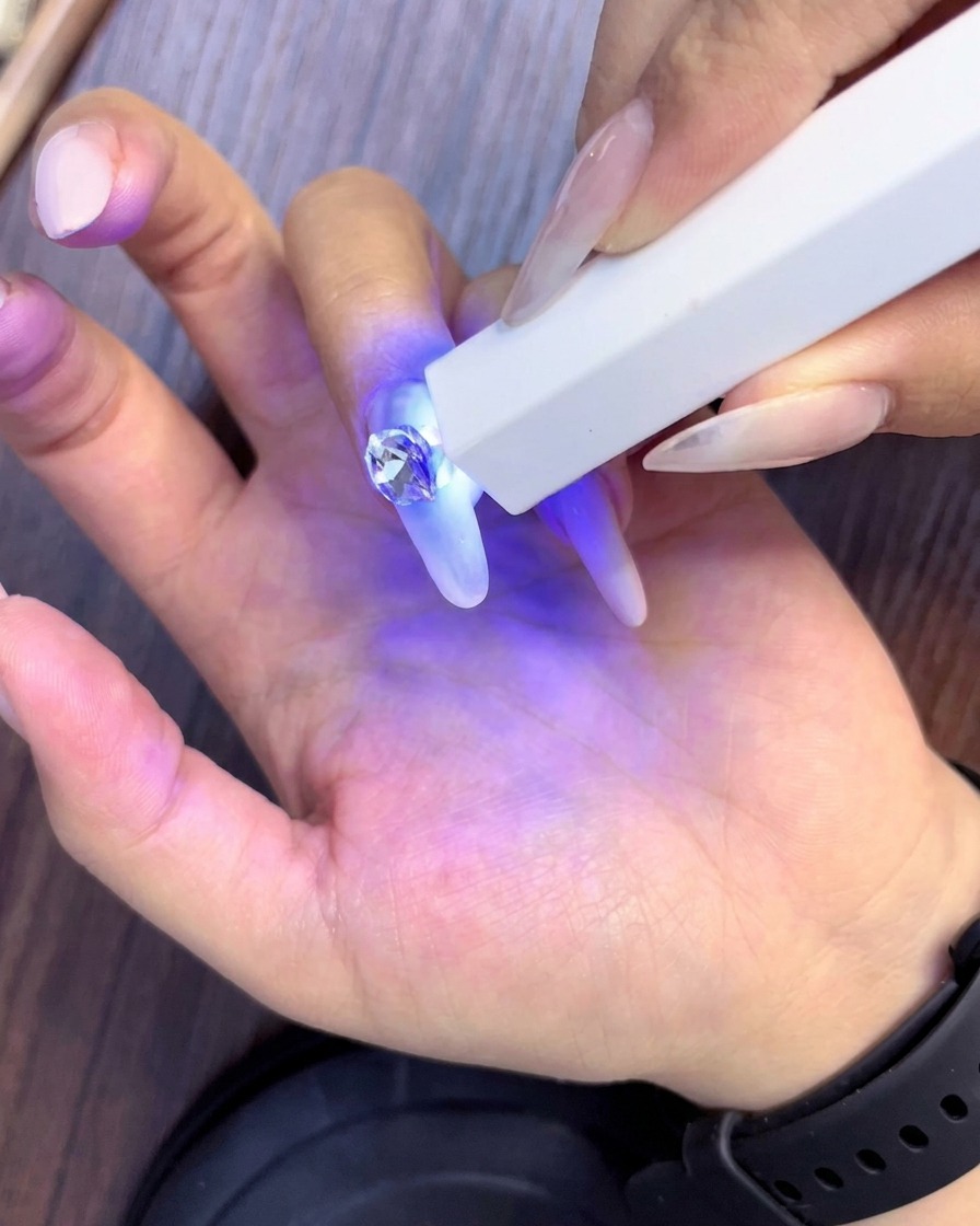 Une lampe UV portable catalysant les strass nouvellement placés autour du cristal central principal sur un ongle en forme damande.