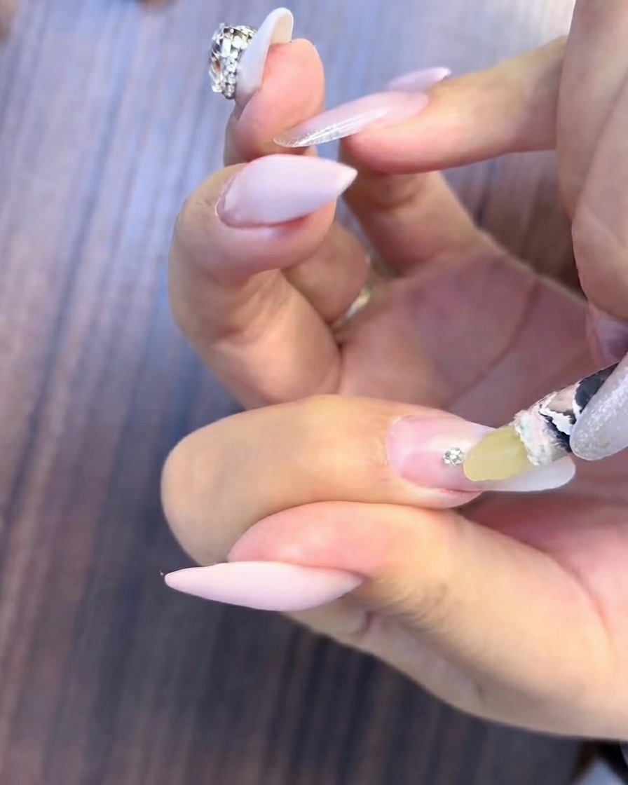 Un pinceau fin appliquant un gel de comblement transparent autour de la base dun petit groupe de strass sur un ongle dégradé.