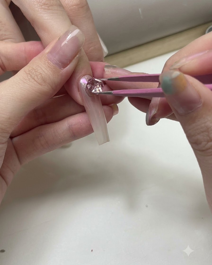 Une paire de pinces positionnant des cristaux roses et transparents étincelants sur une capsule dentraînement transparente.