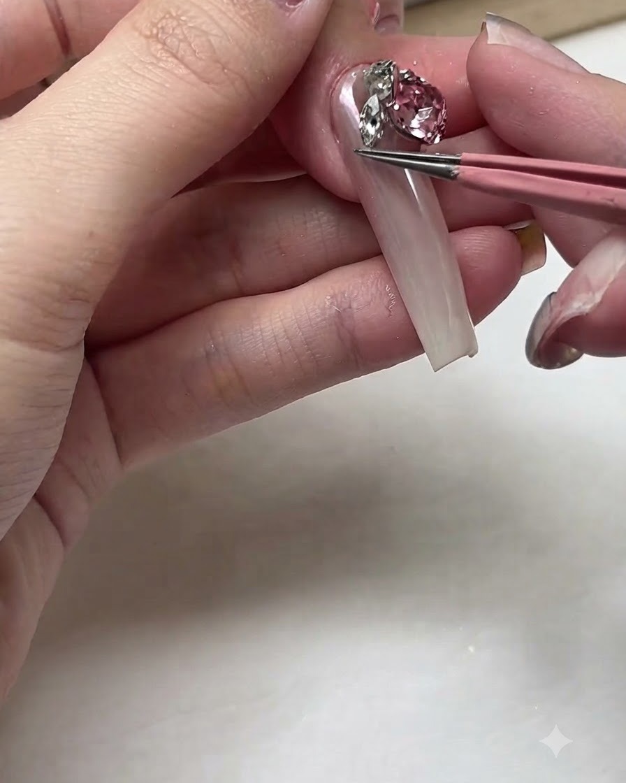 Une paire de pinces roses plaçant un grand strass en cristal rose étincelant sur un long lit unguéal.