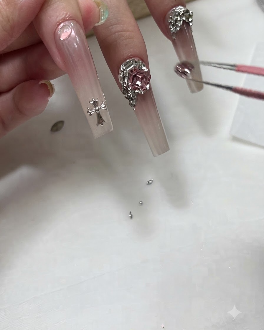 Une prothésiste ongulaire utilisant des pinces pour placer un petit charm en cristal près de la base dun long ongle ombré.
