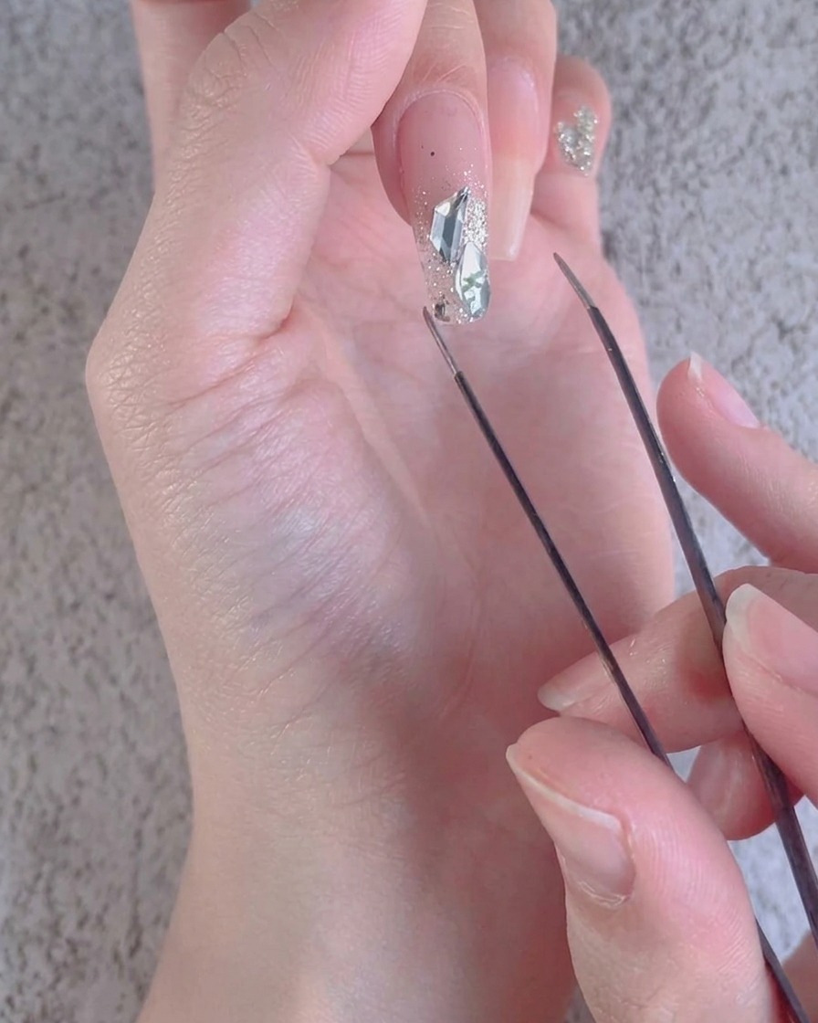 Gros plan dune pince ajustant de petits accents de diamants concassés autour de pierres plus grandes sur un ongle.