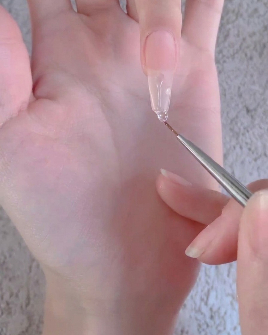 Un pinceau liner tirant une perle de gel transparent vers le bas sur la longueur dune longue extension dongle artificiel.
