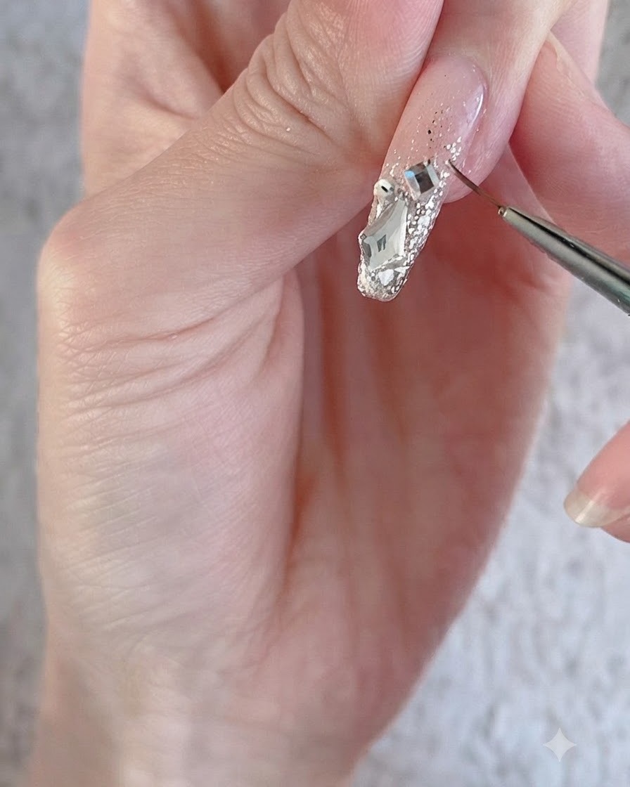 Un pinceau liner fin contournant de grands strass de cristal étincelants et des charms sur une surface dongle décorée.