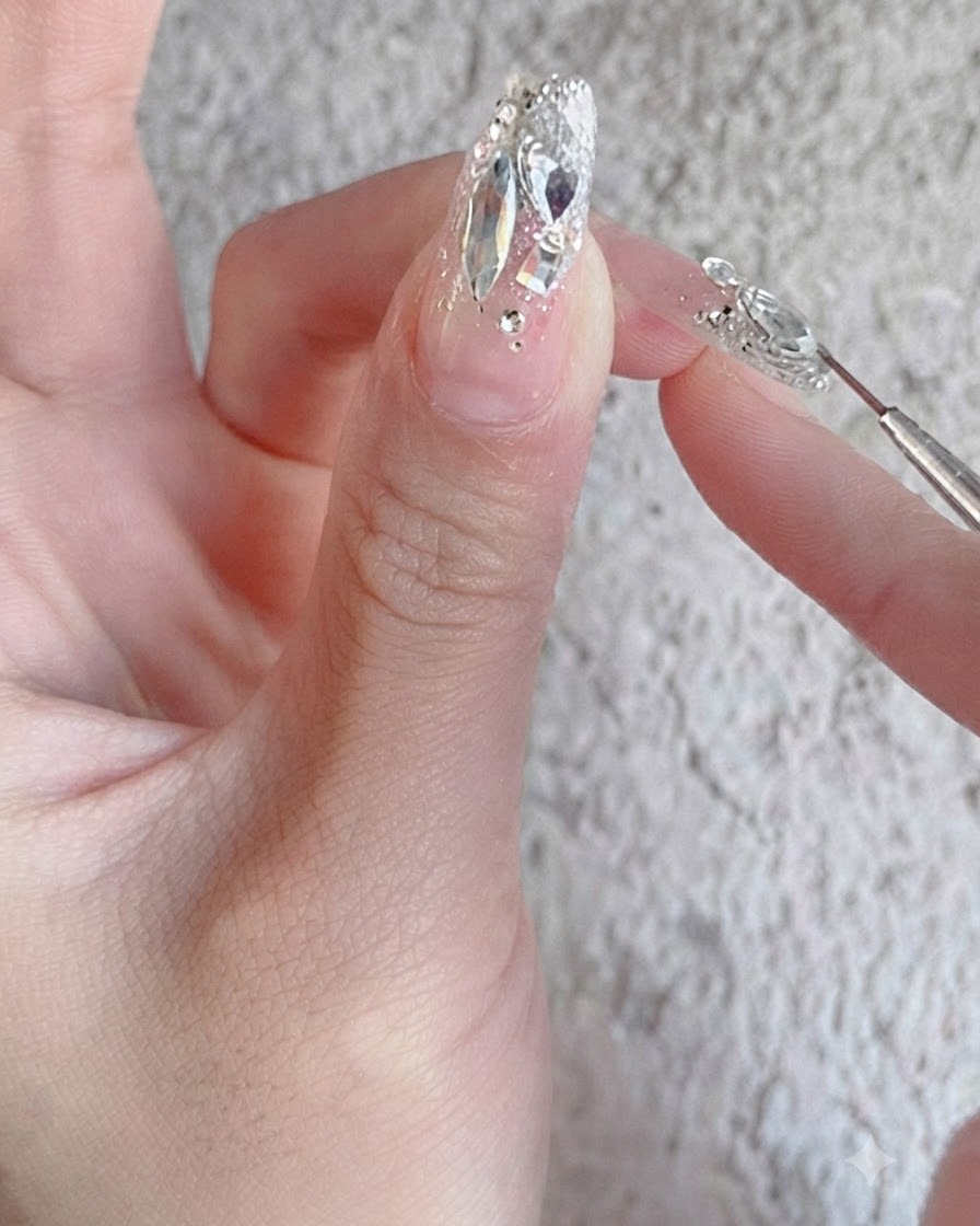Un pinceau à ongles appliquant un top coat de renfort brillant sur un design dongle avec strass entièrement terminé.