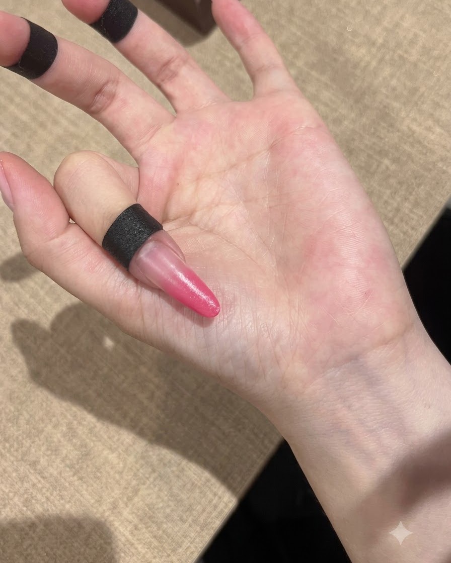 Une main positionnée sous une lampe UV compacte pour catalyser les ongles en dégradé rose.
