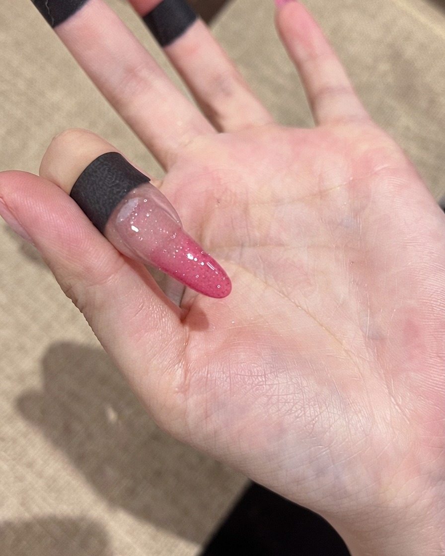 Gros plan sur un ongle montrant de fines particules de paillettes réfléchissantes sous un éclairage intérieur standard.