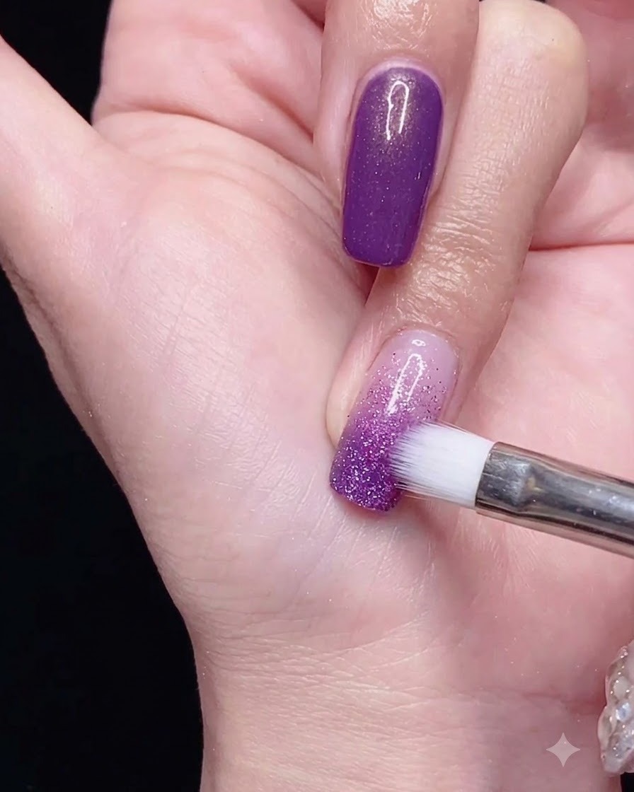 Un pinceau à dégradé estompant le vernis semi-permanent violet vers le bas sur longle pour un effet ombré lisse.
