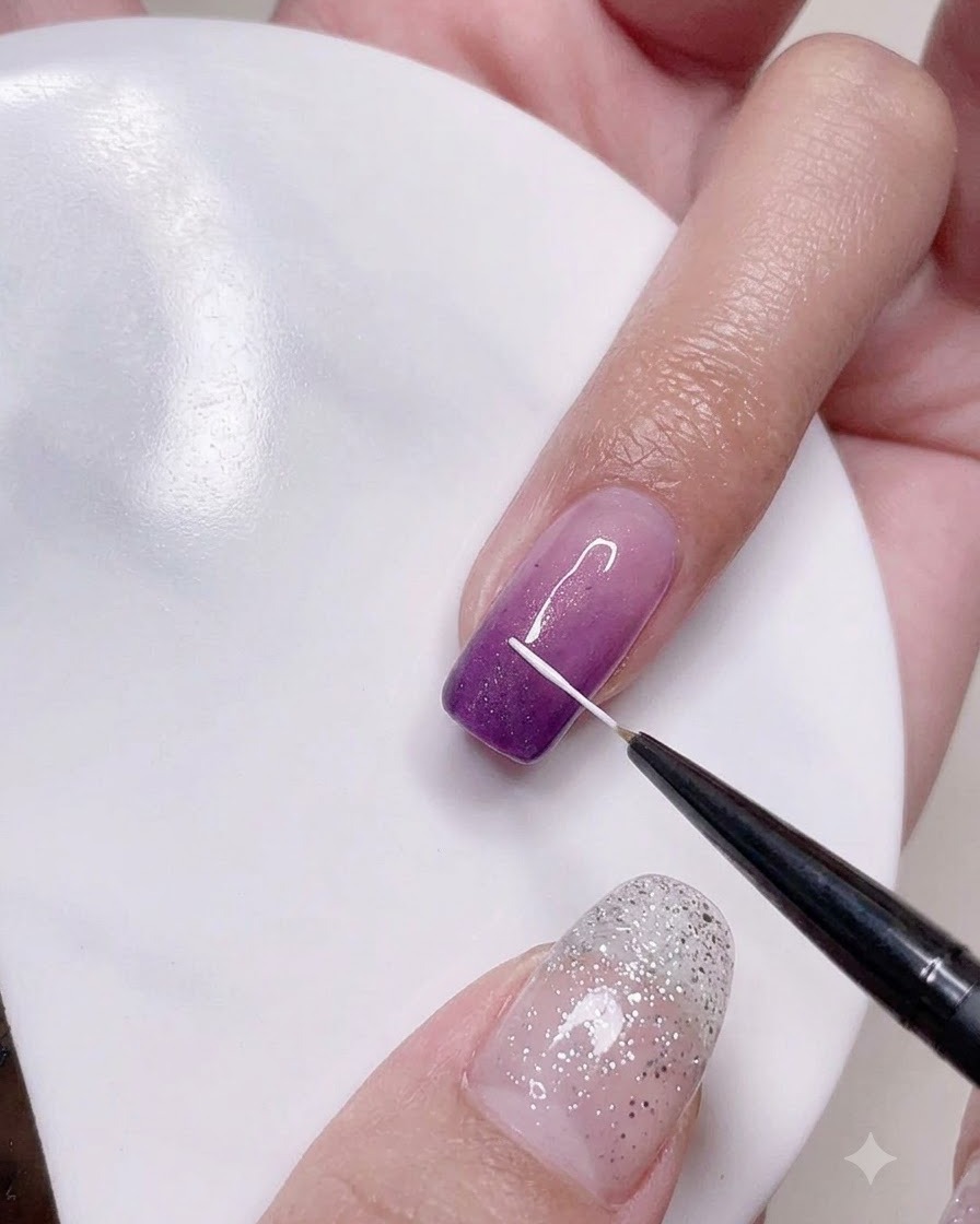 Un pinceau liner fin dessinant des lignes blanches verticales précises sur la surface de longle ombré violet.