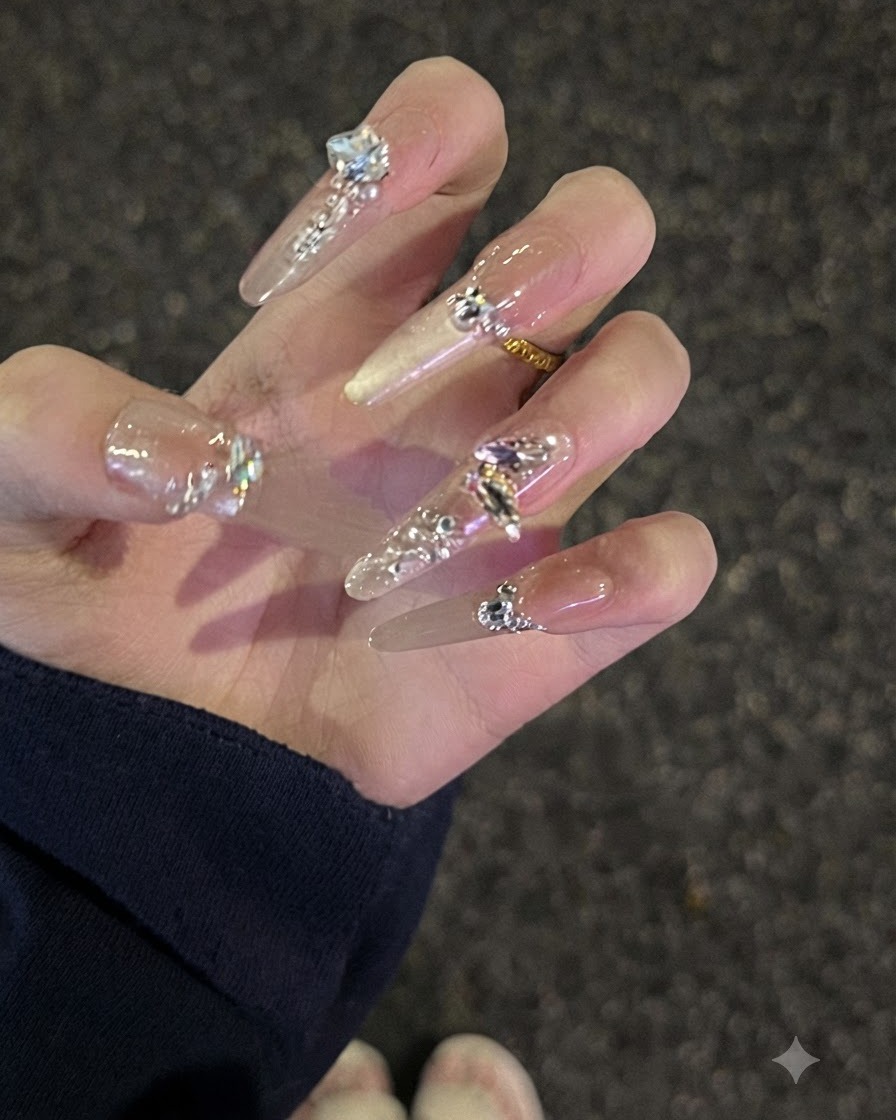 Une vue en gros plan dune main avec de longs ongles nudes parsemés de strass et légèrement courbés pour montrer le profil.