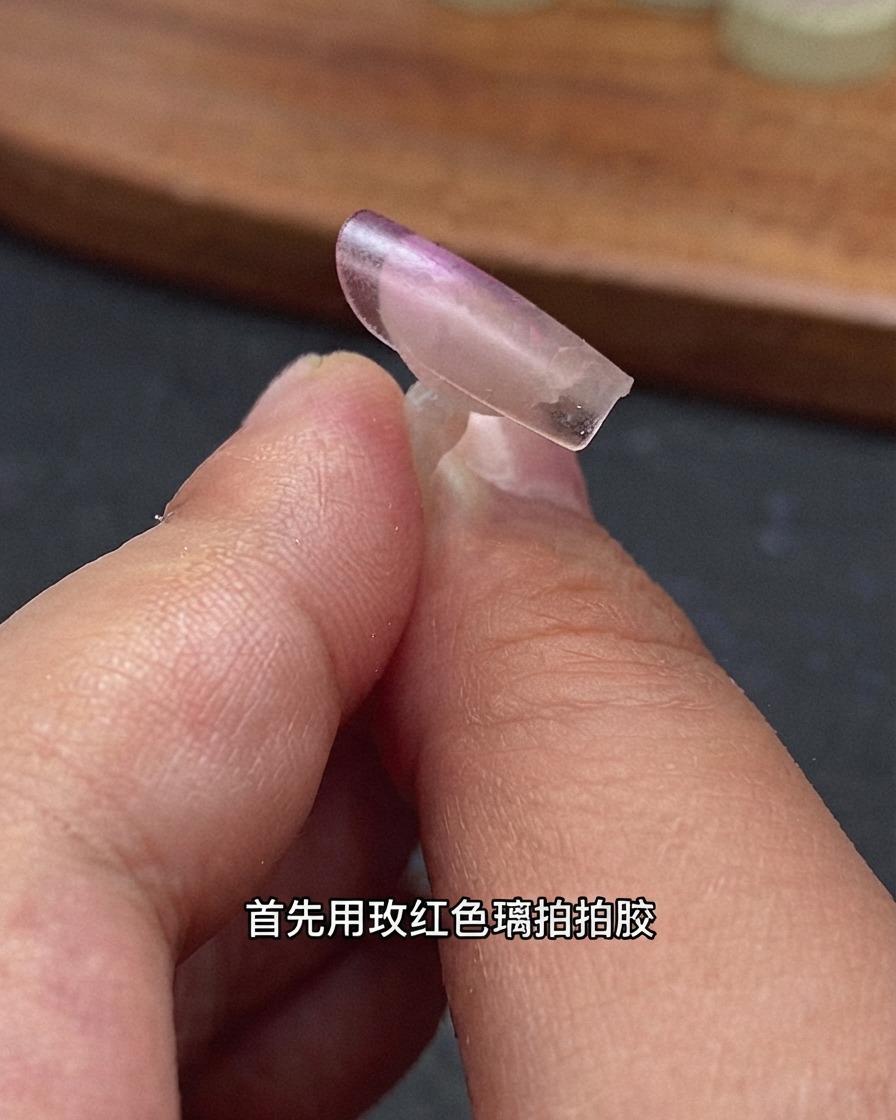 Gros plan dune capsule dongle transparente tenue par des doigts avec du gel verre rose rouge appliqué sur le bord arrière.