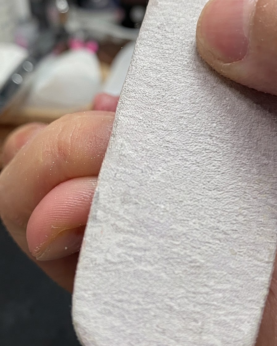 Main tenant un bloc polisseur blanc limant légèrement la surface dun ongle naturel.