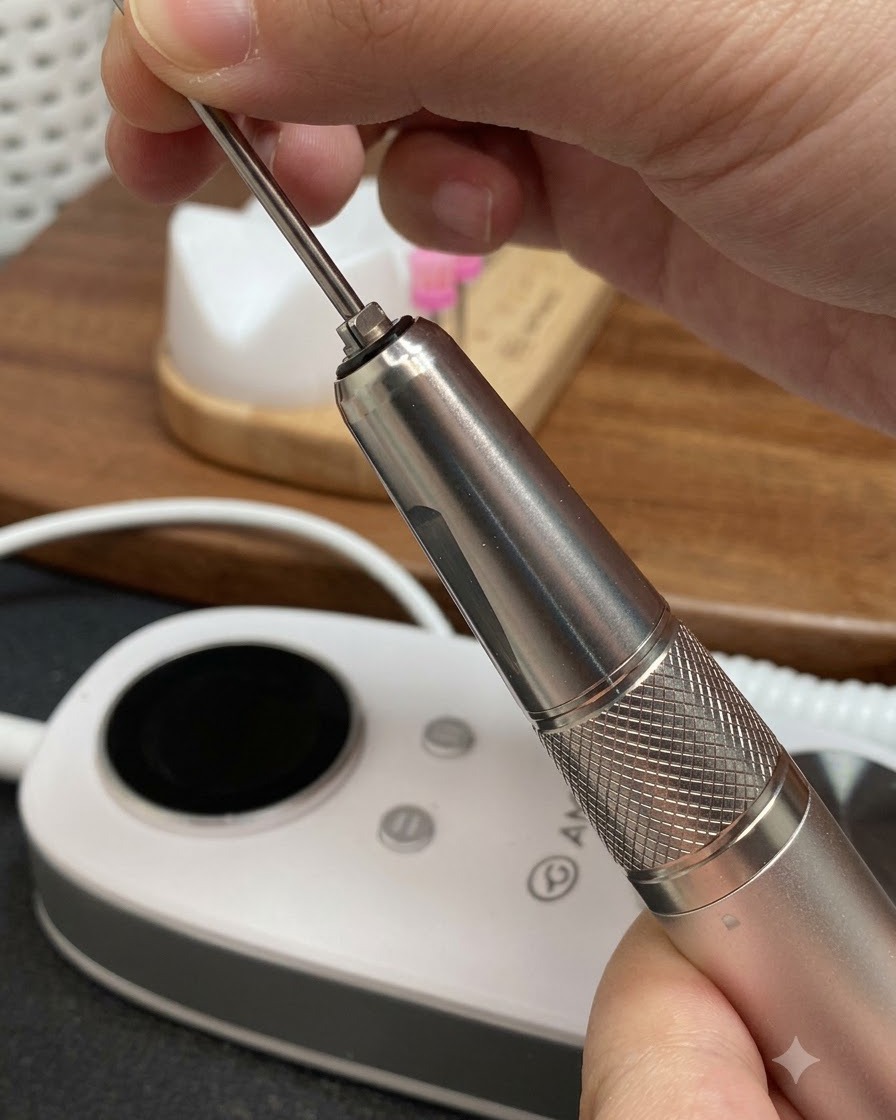 Mains insérant une fraise métallique conique longue dans la pièce à main dune ponceuse à ongles électrique.