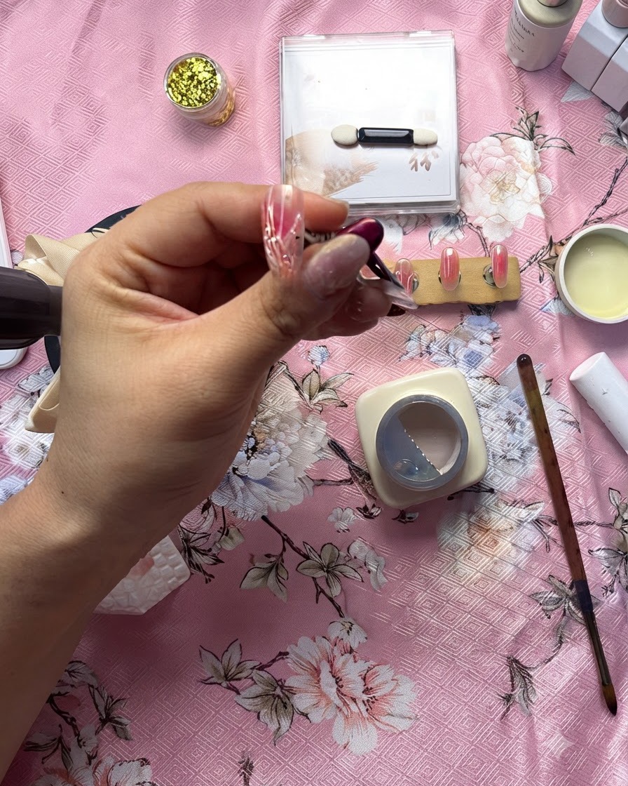 Gros plan détaillé dune prothésiste ongulaire utilisant un pinceau fin pour appliquer une ligne de gel transparent en relief sur un design de cœur blanc.