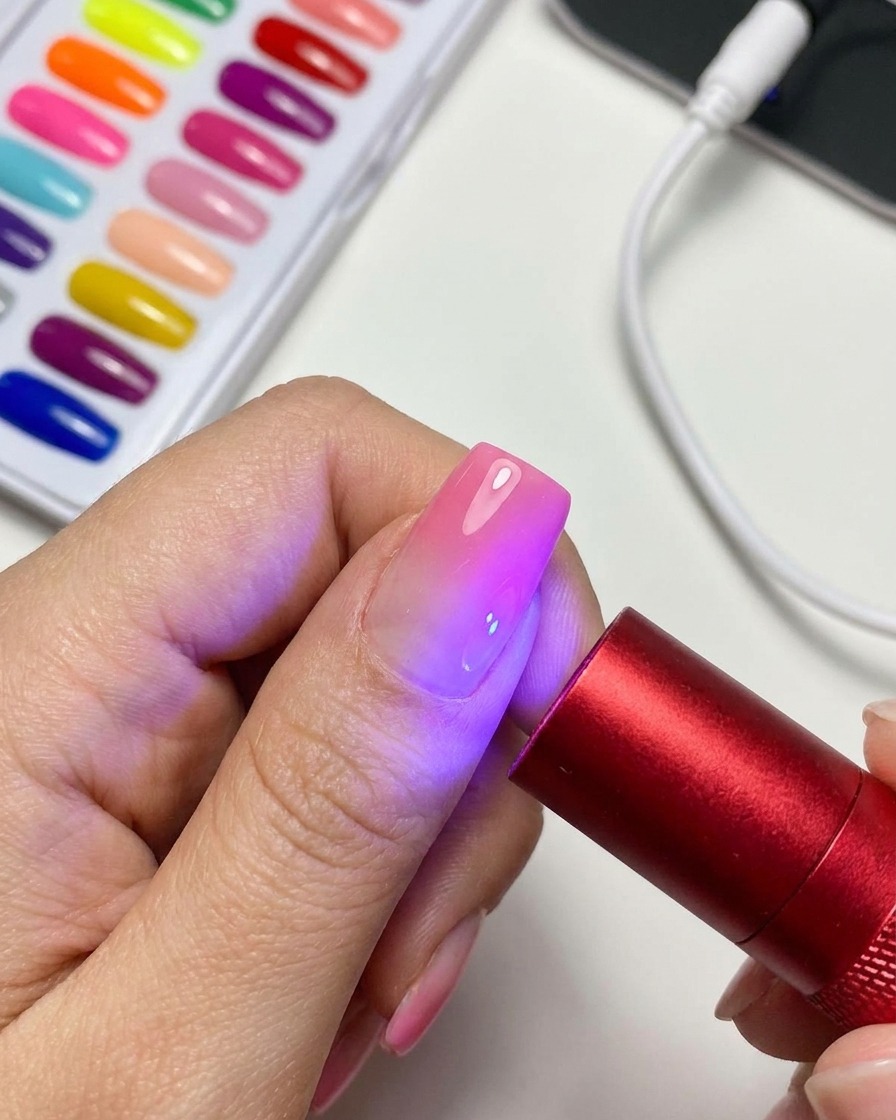 Une lampe UV/LED rouge portable éclairant un ongle fini avec du gel magnétique œil de chat.
