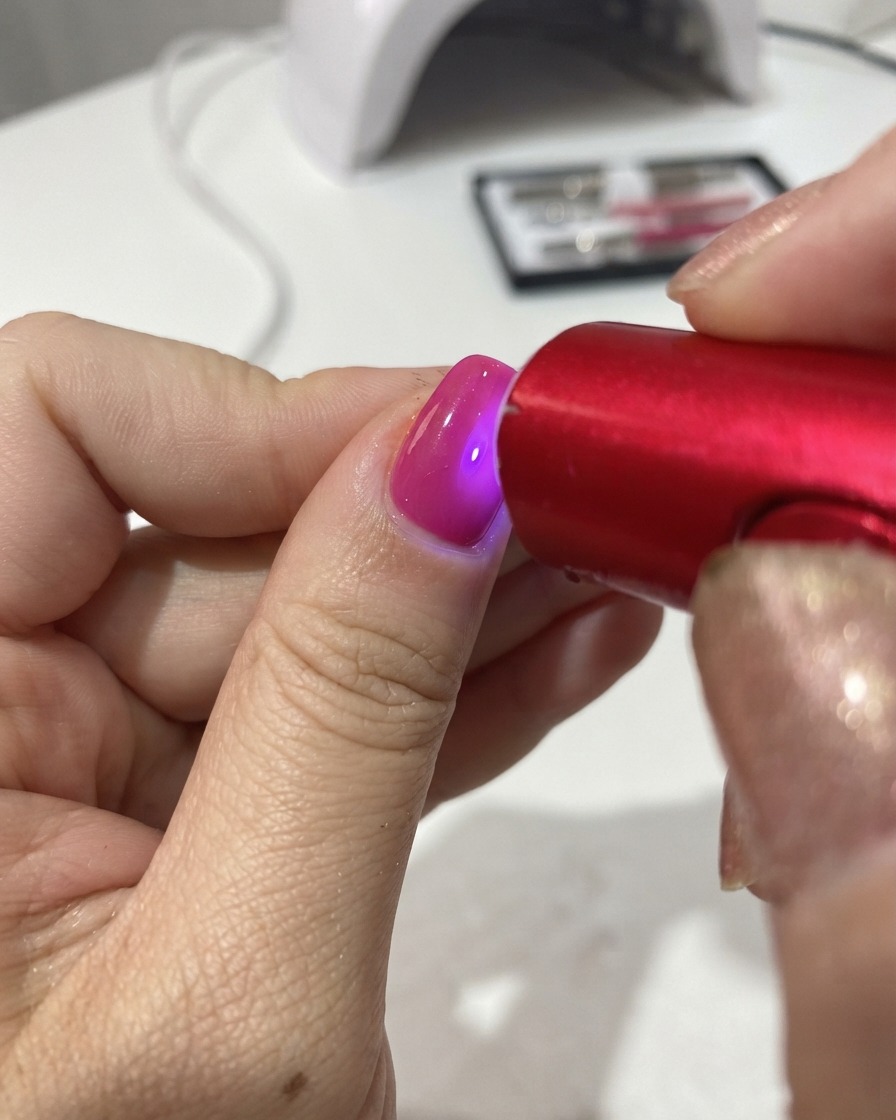 Une lampe UV/LED rouge portable catalysant le vernis gel sur un ongle.