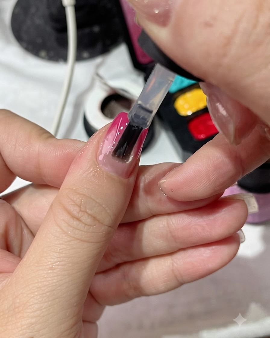 Un pinceau à vernis appliquant une couche de finition transparente uniformément sur un ongle manucuré en dégradé.