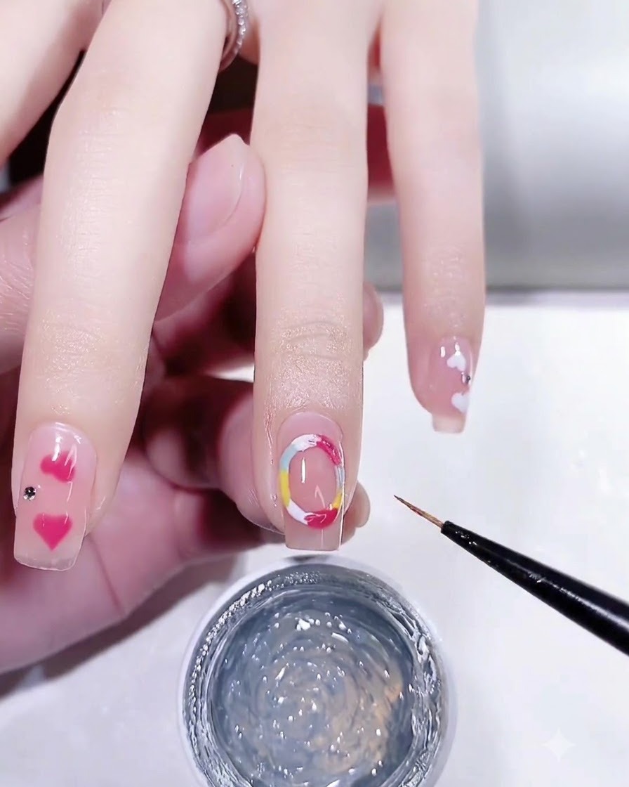 Un pinceau fin appliquant du gel de modelage 3D transparent sur les cercles colorés peints sur un ongle.