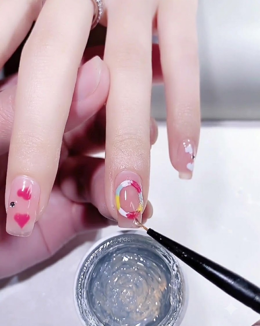 Un pinceau de nail art fin appliquant un top coat brillant sur un ongle manucuré avec des détails de points colorés.