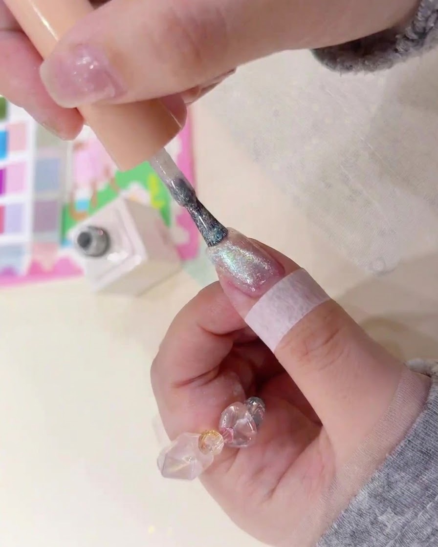 Un pinceau appliquant un gel ambré magnétique scintillant sur un ongle naturel.