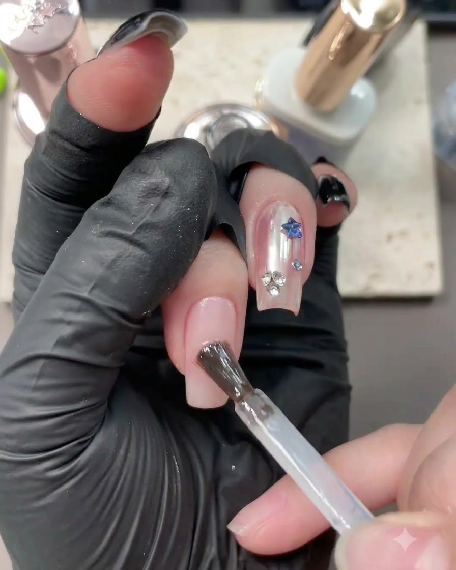 Un pinceau appliquant un gel de base transparent sur un ongle nude neutre avec du nail art existant.