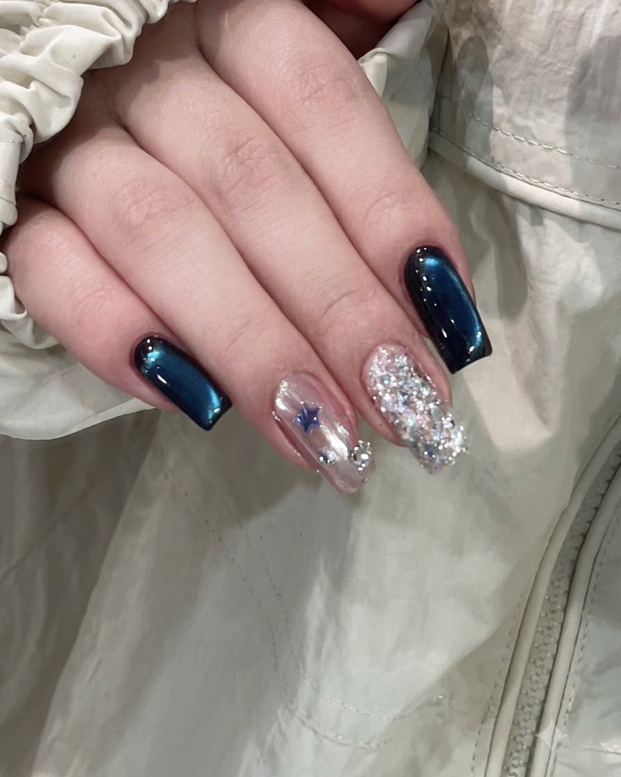 Une main finie montrant des ongles cat-eye bleu profond à côté dun ongle daccentuation orné détoiles et dun ongle entièrement pailleté.