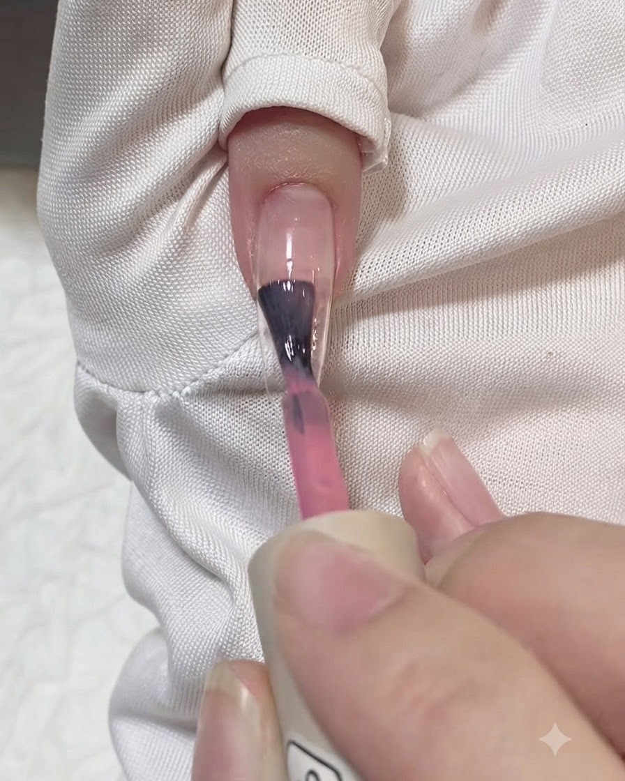 Un pinceau appliquant un trait de gel rose translucide au centre dune extension dongle transparente.