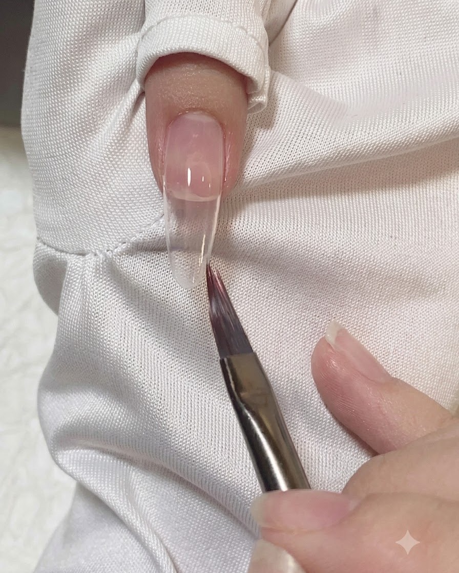 Un pinceau plat lissant et estompant les bords du gel rose sur un onglet.