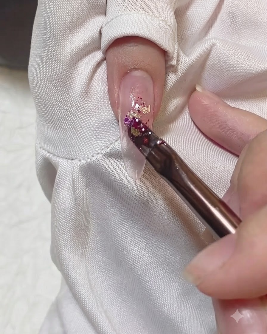 Un pinceau appliquant un amas de paillettes colorées au centre dun ongle.
