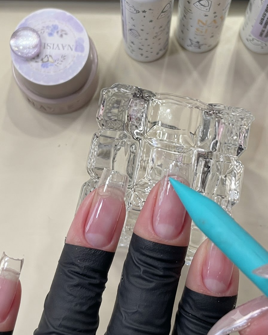 Un pinceau bleu appliquant une base coat peel-off transparente sur le contour des cuticules dun ongle naturel.