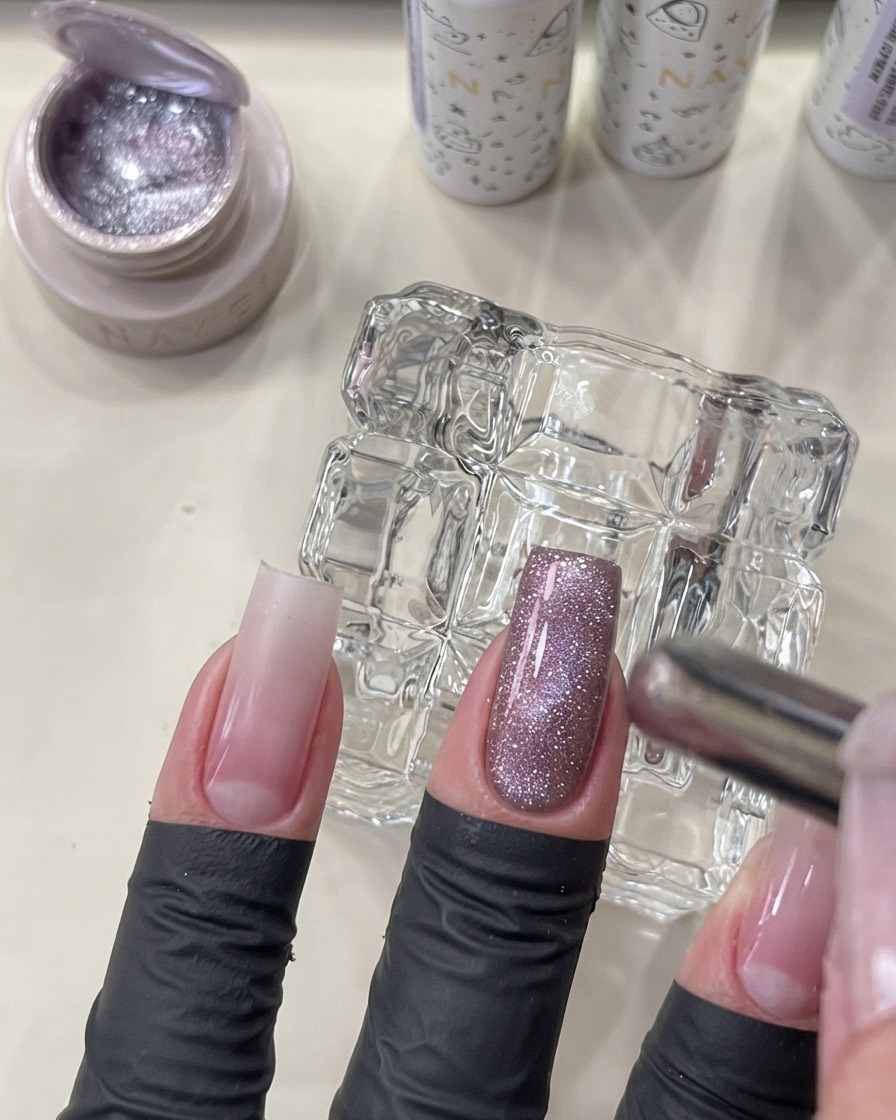 Un outil aimanté tenu près dun ongle manucuré pour façonner le gel cat eye en un effet perle de verre lumineux.