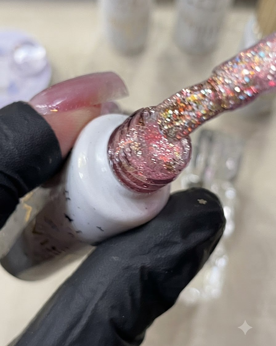 Un pinceau tenant du gel à paillettes orange chaud au-dessus dun ongle.