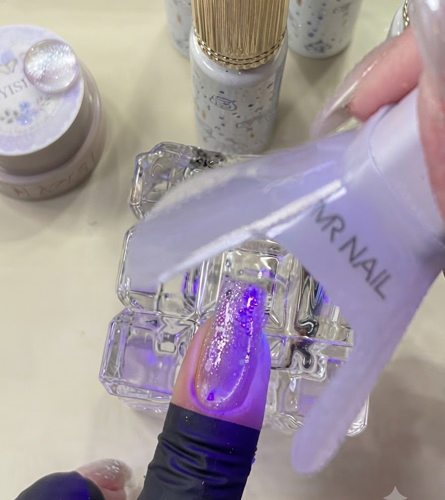 Une mini lampe UV catalysant un ongle décoré sous une lumière violette.
