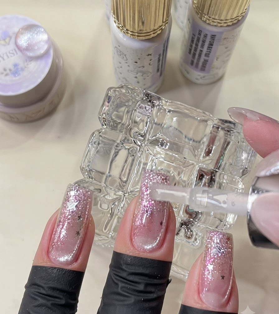 Un pinceau appliquant le top coat final sur des ongles achevés de style galaxie.