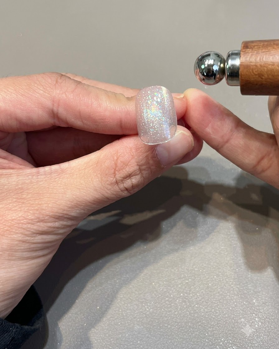 Un aimant sphérique tenu près dun ongle en gel cat eye rose doré chatoyant pour façonner la bande lumineuse.