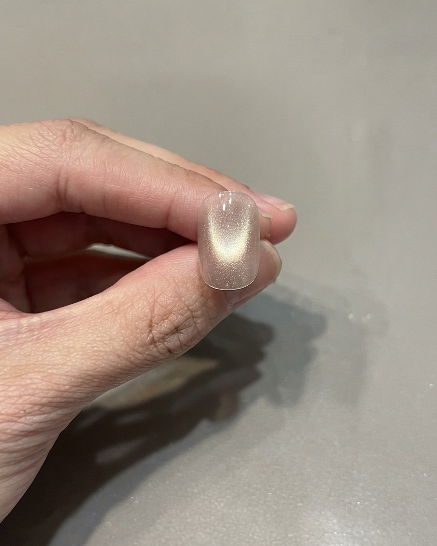Un ongle manucuré unique présentant un vernis cat eye rose doré catalysé avec un reflet lumineux centré.
