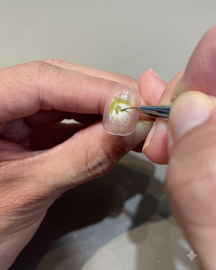 Vue rapprochée dun pinceau fin remplissant minutieusement de gel vert avocat pour créer des feuilles de fraise sur un ongle nude rosé.