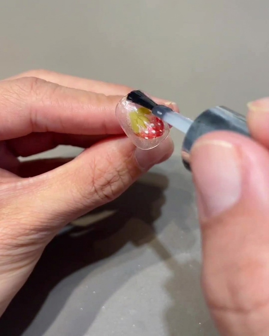 Un pinceau appliquant un top coat transparent sur un ongle décoré.