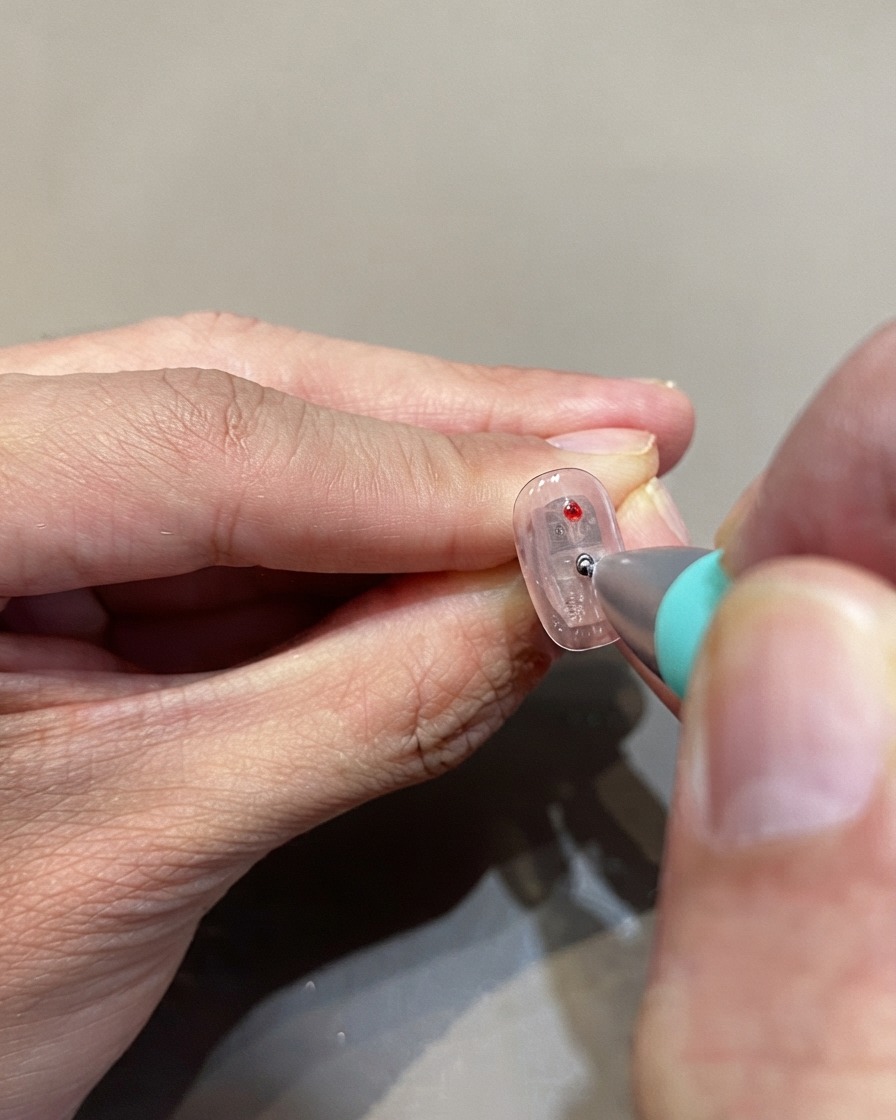 Un outil de dotting plaquant des pois en gel glass rouge sur une surface dongle transparente.