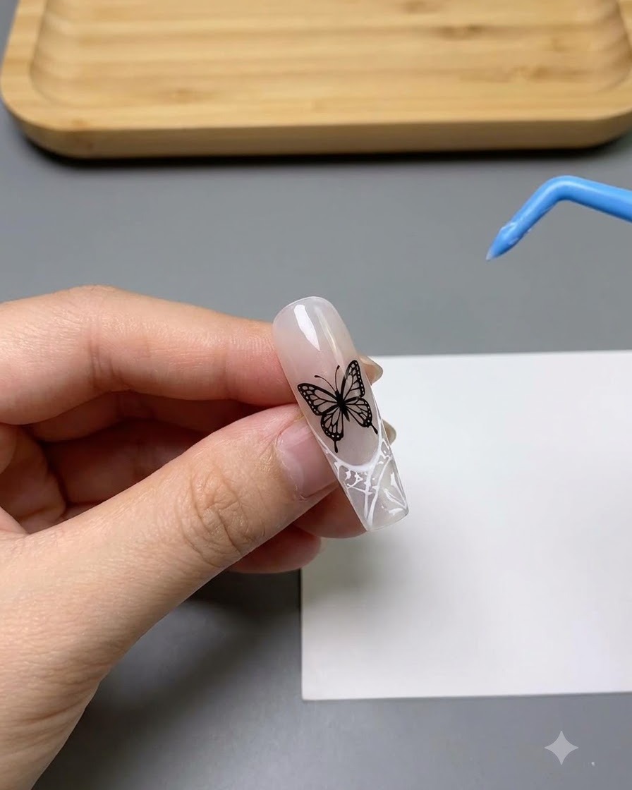 Gros plan dun ongle décoré dun motif de papillon ajouré blanc très détaillé.